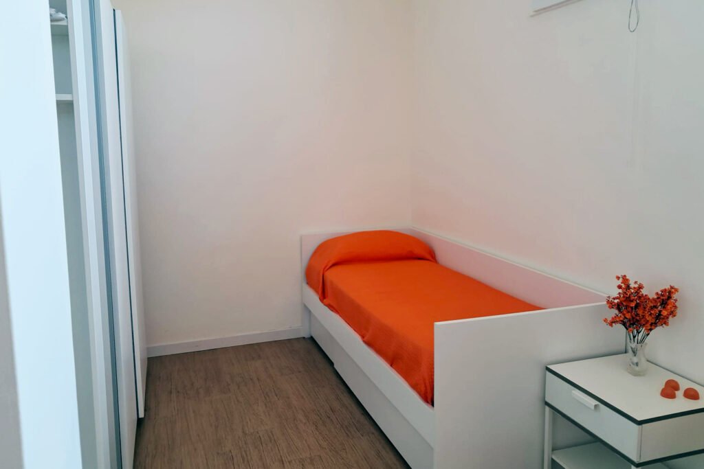 un letto singolo con il suo armadio nello spazio della mansarda condivisa